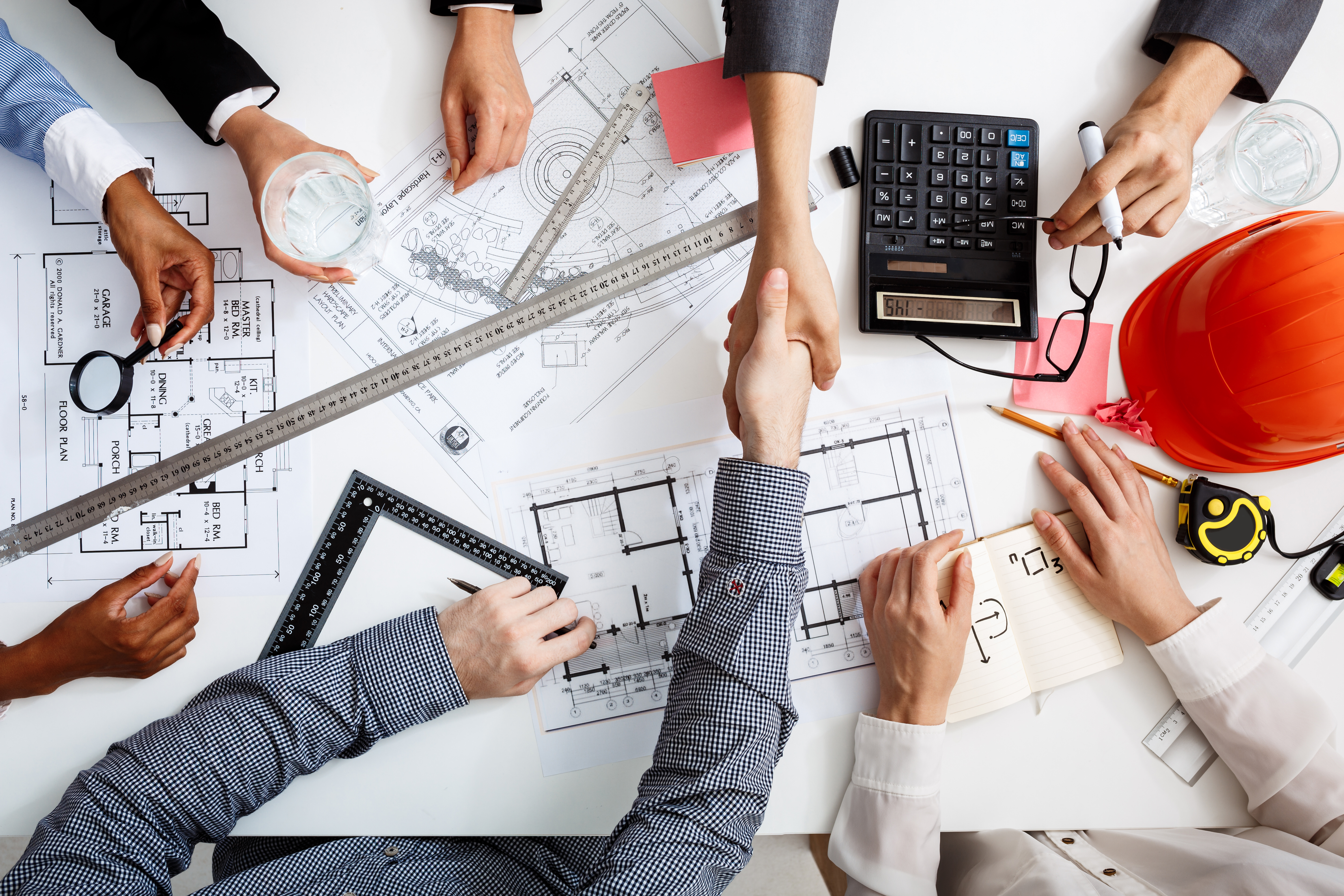 Tavolo di lavoro con planimetrie, strumenti tecnici e stretta di mano